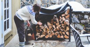 Woman in sweater placing wood into a firewood holder.