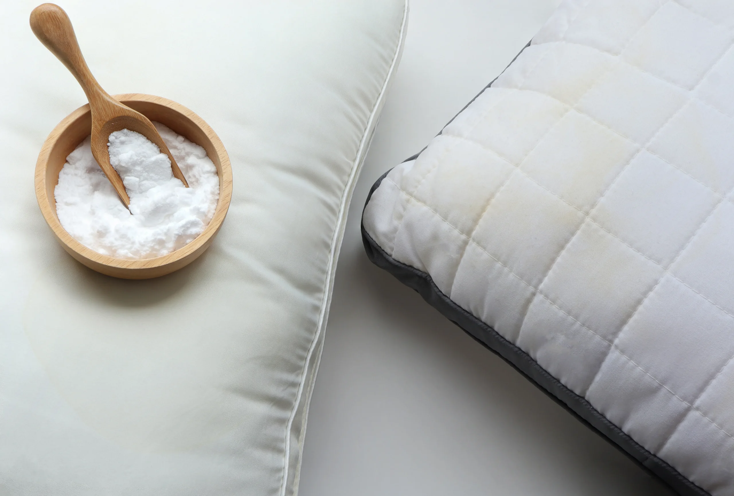 A wooden bowl and scoop filled with baking soda sitting next to a white mattress pad, a common home remedy attempt for pest control.
