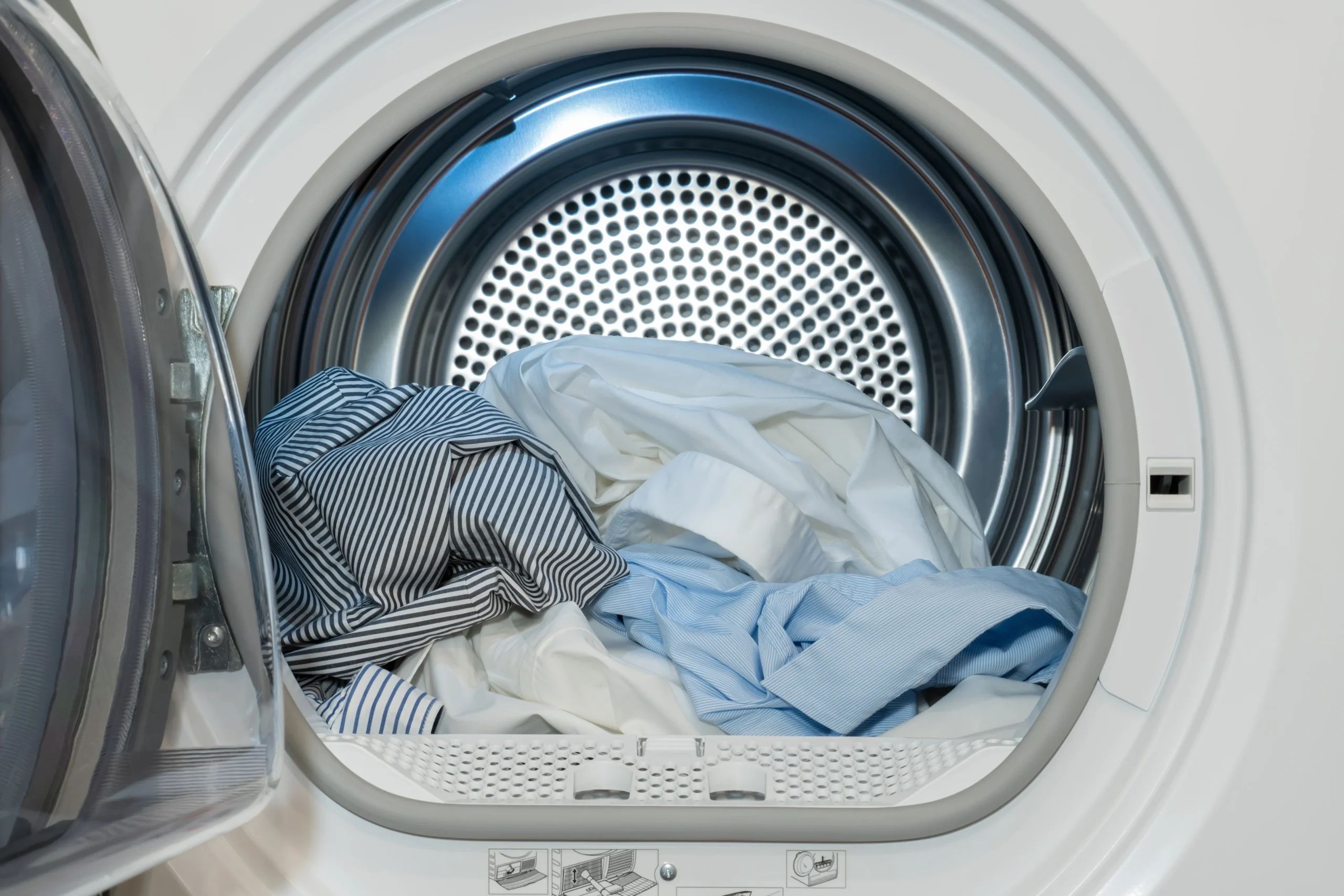 An open, front-loading dryer filled with shirts and bedding being dried on high heat to eliminate bed bugs.
