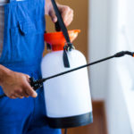 Exterminator in blue overalls with a portable spray canister.