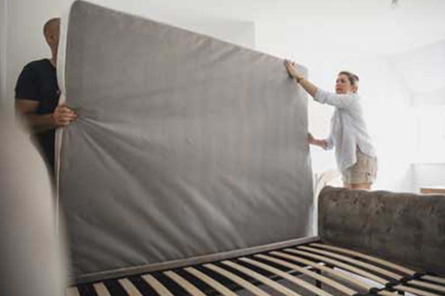 a man and woman pull up a mattress to check for bed bugs underneath