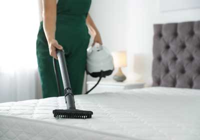 a woman steam cleans a bed to eliminate bed bugs