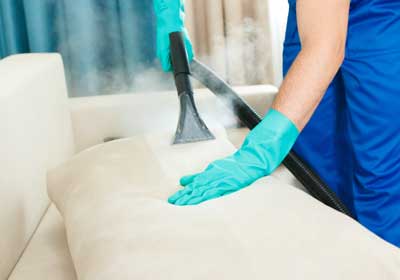 a person steam cleans a couch to get rid of bed bugs