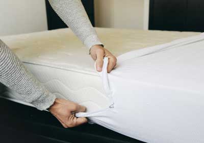 a man puts a mattress cover on his bed for bed bug prevention