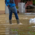A photo of someone wading through high flood waters in a residential neighborhood.